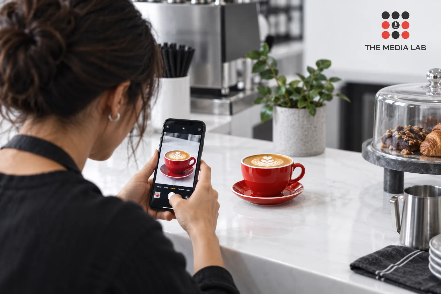 Cafe owner photographing a red cup for social content — editorial illustration for The Media Lab.