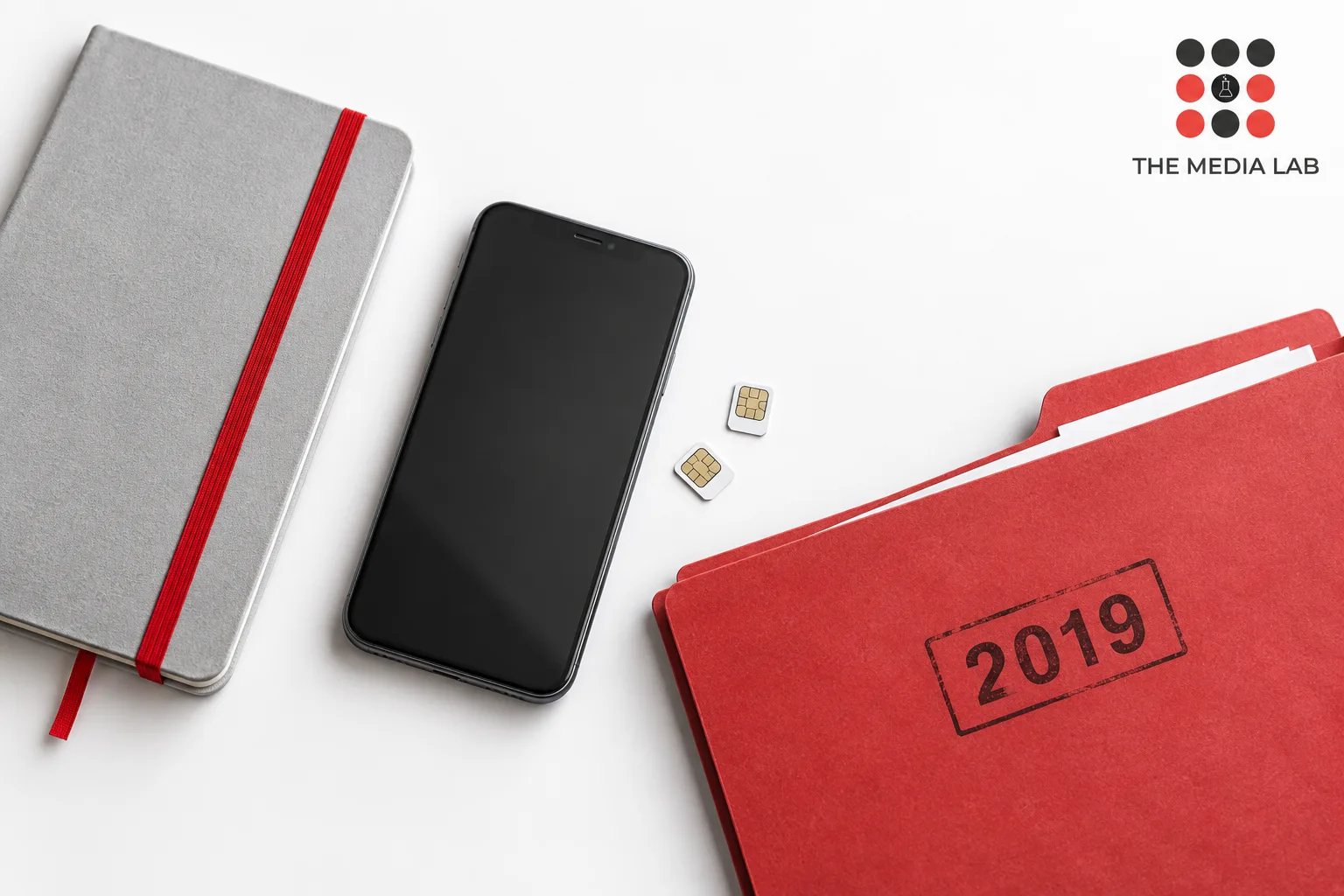 Smartphone and two SIM cards beside a 2019 folder, illustrating The Media Lab’s guide to devices and digital users.