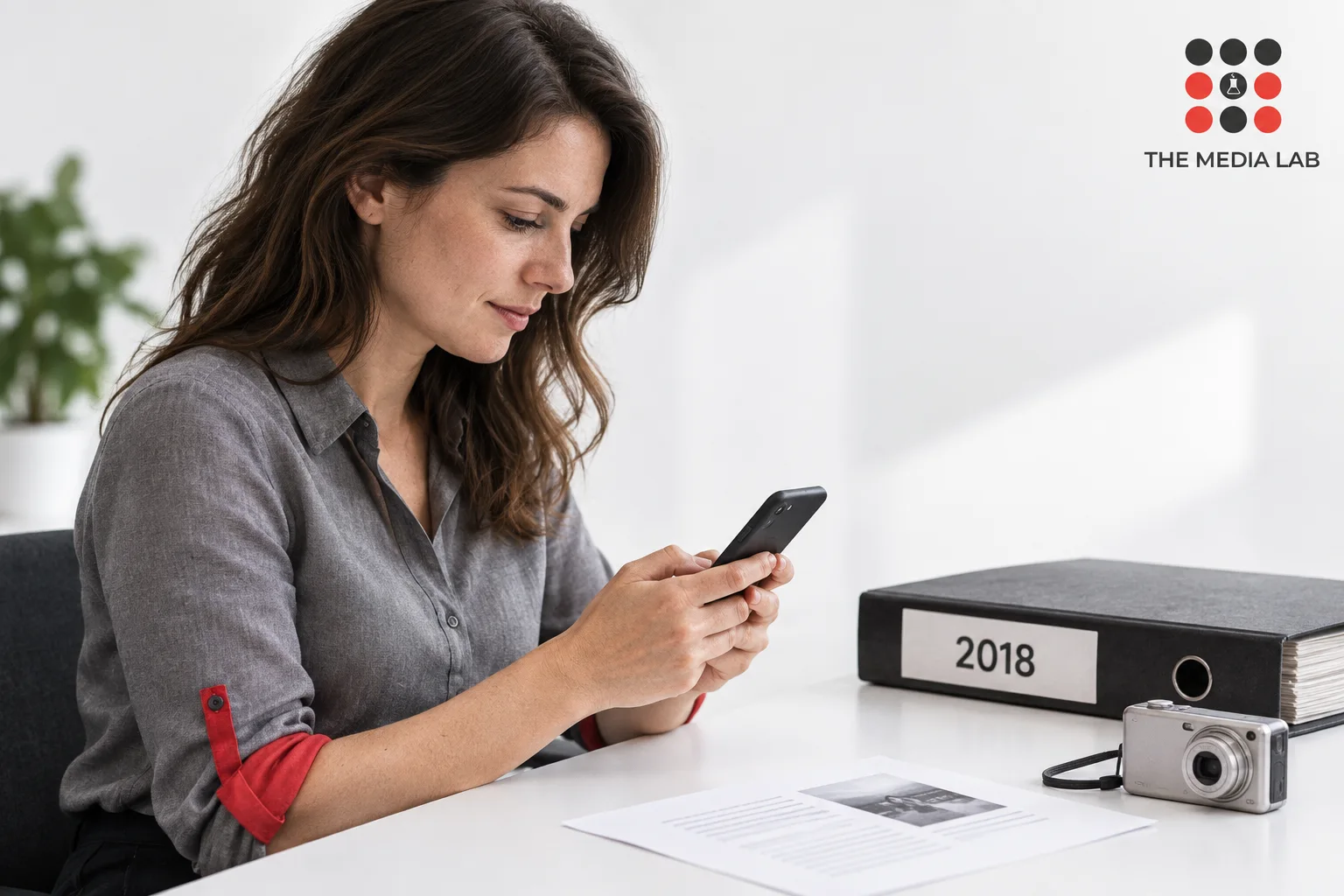 Professional reviewing a phone beside a 2018 archive folder, illustrating The Media Lab’s historical social media guide.