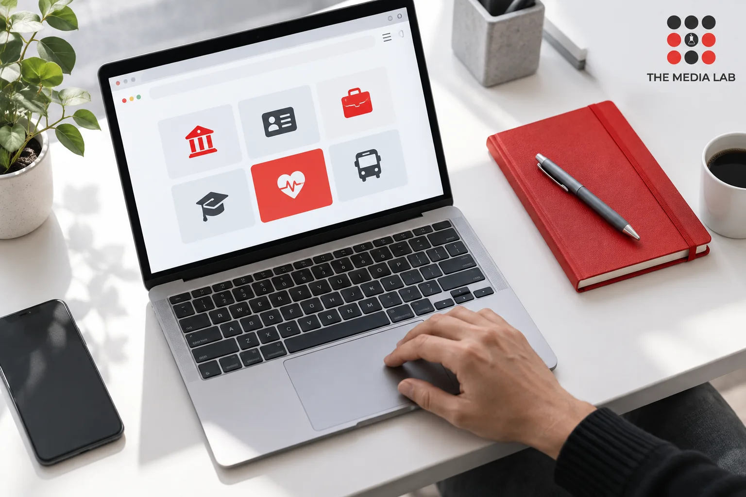 Laptop with service navigation tiles and a red notebook, illustrated for The Media Lab’s UAE website guide