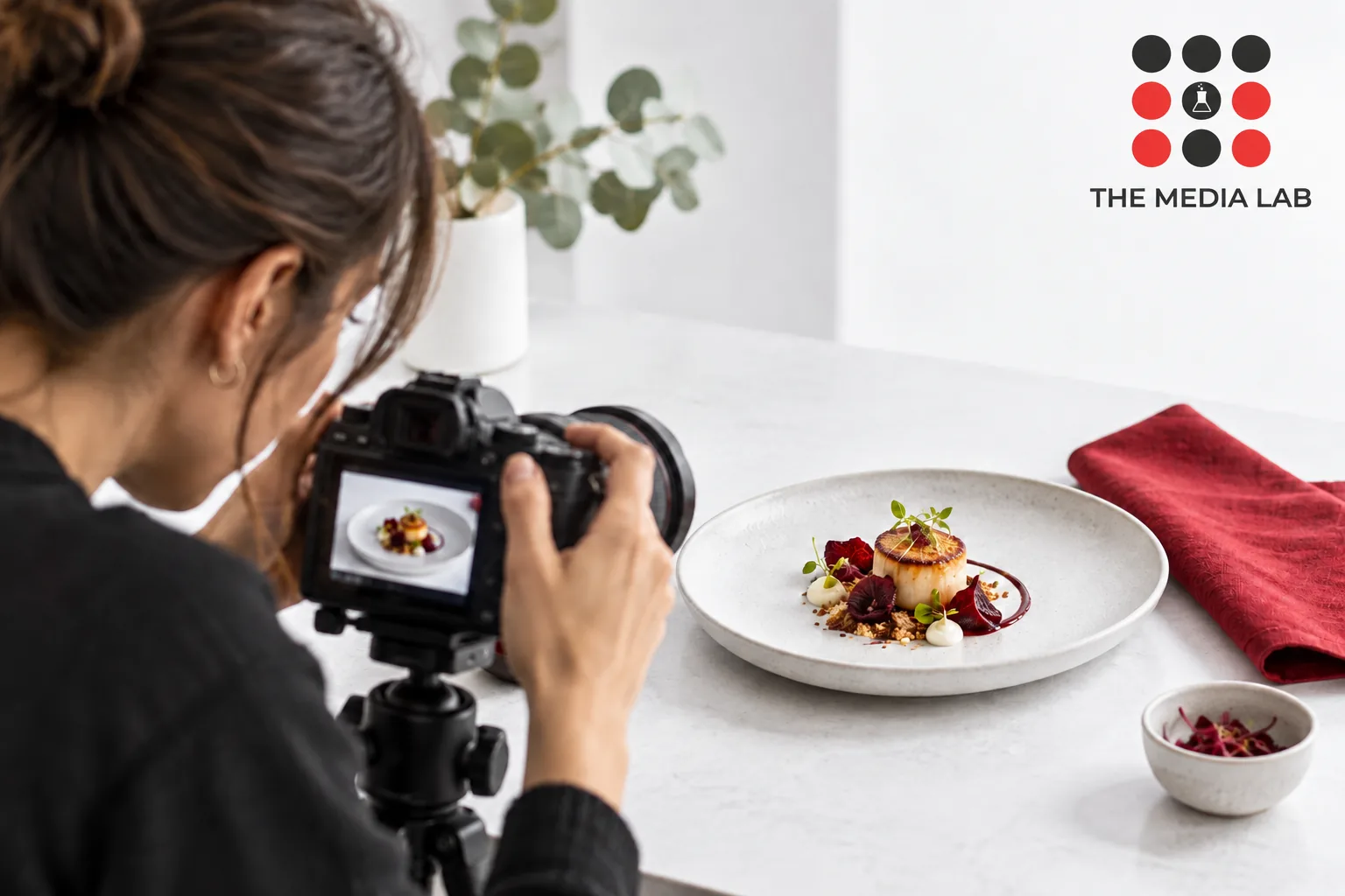 Niche food creator filming a carefully plated small dish in white studio with red napkin — The Media Lab