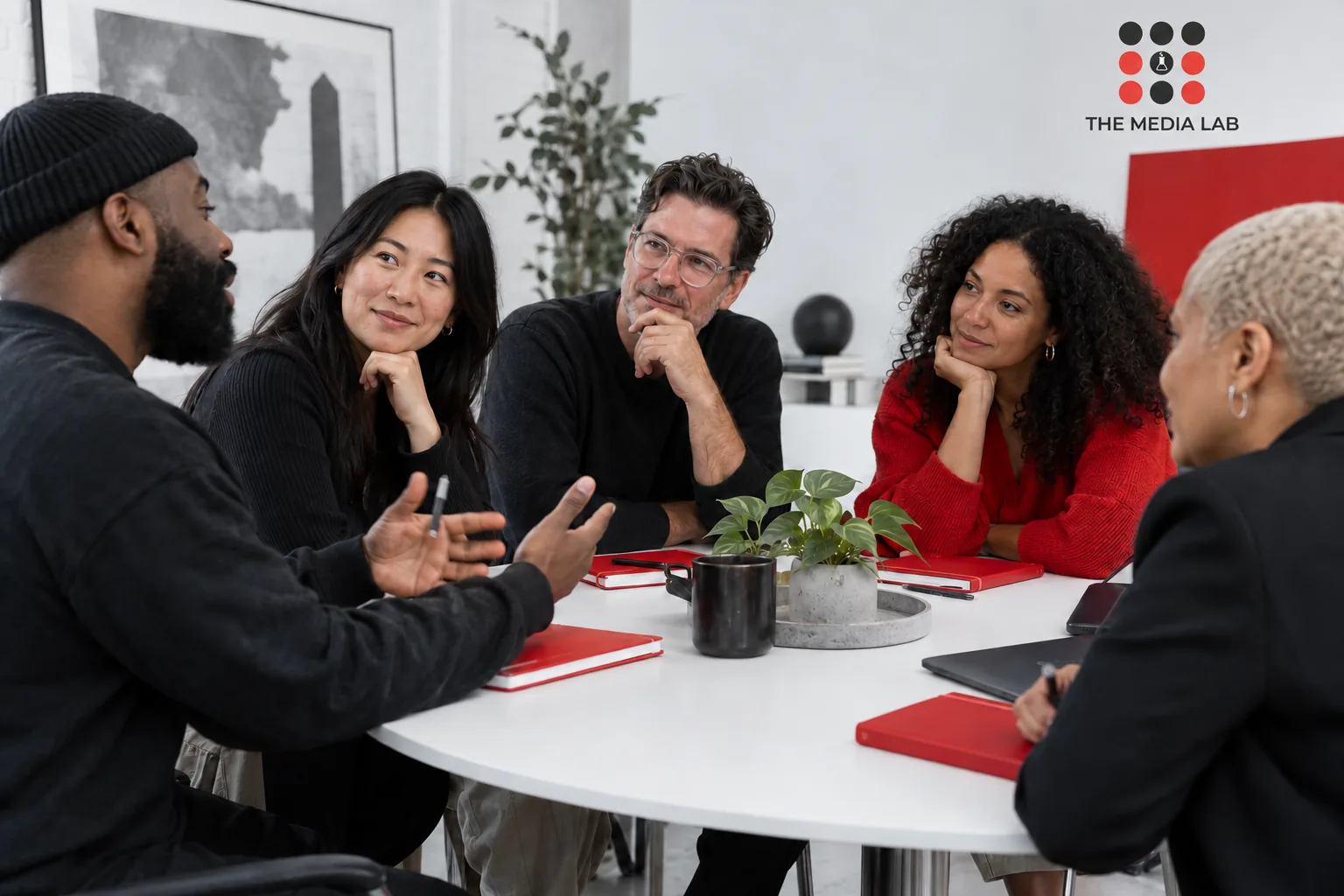 Small diverse business community in a roundtable conversation, white studio, red notebooks — The Media Lab