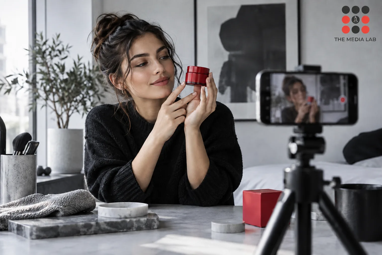New creator filming a small red skincare product with phone on tripod — The Media Lab